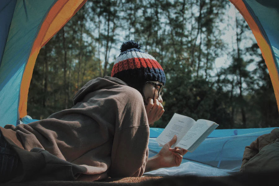 person reading inside a tent with a view to the trees outside