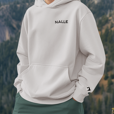 Man wearing a gray hoodie with the Nalle logo on standing on a mountain.