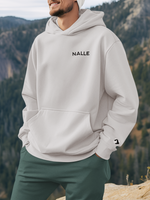 Man wearing a gray hoodie with the Nalle logo on standing on a mountain.