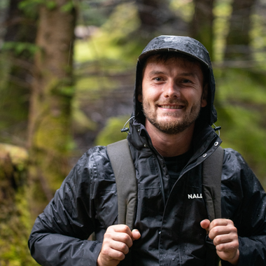 Man wearing a navy blue rain jacket with the Nalle logo hiking in a rainy forest