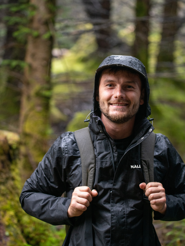 Man wearing a navy blue rain jacket with the Nalle logo hiking in a rainy forest