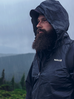 Man wearing a navy blue rain jacket with the Nalle logo hiking in a rainy forest