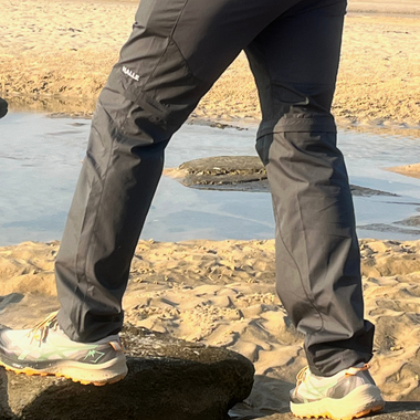 Man wearing gray hiking pants with Nalle on the thigh hiking on a beach.