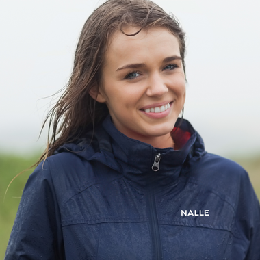 Girl with damp hair wearing a navy blue rain jacket with Nalle logo in the outdoors.