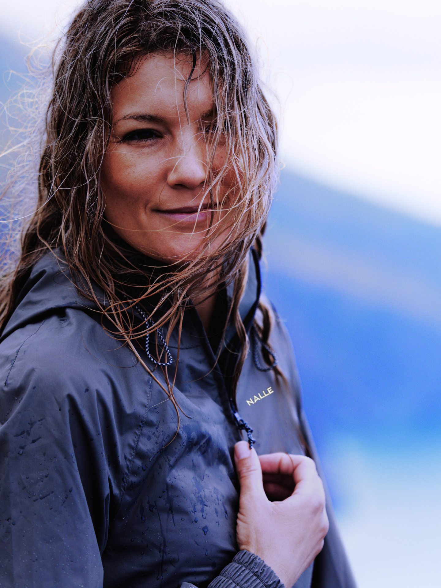 Girl with damp hair wearing a navy blue rain jacket with Nalle logo in the outdoors.