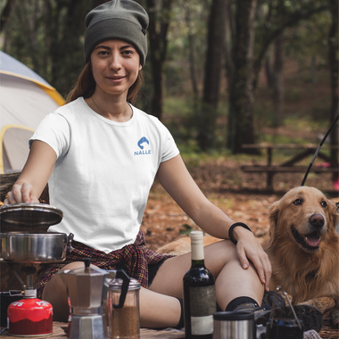 Woman wearing a white t-shirt with the Nalle logo on camping in the forest with a Golden Retriever by her side. 