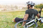 Man sitting on the grass in front of his bike wearing a bike helmet and black Nalle tee with the Mooka wizard on it.