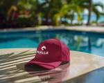 Red cap with Nalle logo on the edge of a pool deck with palm tress in the background