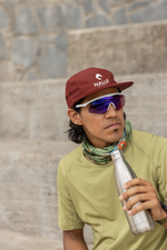 Man wearing a red cap with the Nalle logo on it sitting in front of a wall resting after a hike drinking from a metal water bottle.